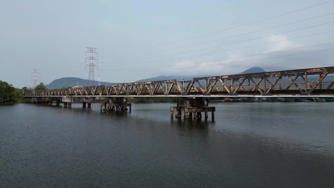 柬埔寨贡布旧铁路桥的无人机镜头。摄像机从河上锈迹斑斑的桥上方的陆地上移开。