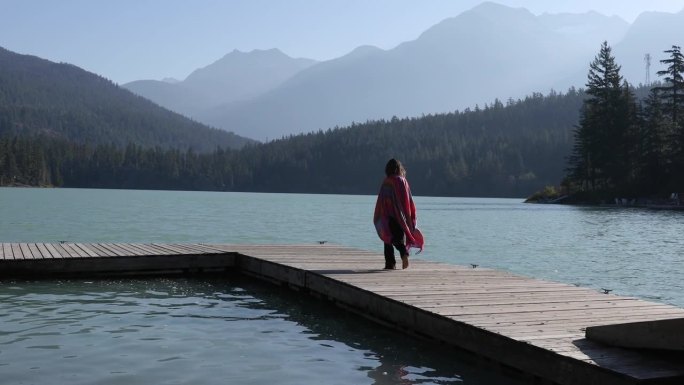 年轻的孕妇沿着湖上的木码头散步