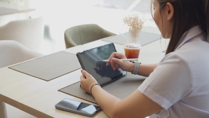 亚洲聪明的女医生穿着制服，用平板电脑和数字笔在咖啡馆工作或在家工作远程会议。医疗健康人的理念。