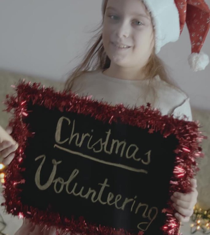 一个微笑的小女孩举着写有“圣诞志愿者”字样的黑板。圣诞志愿概念。垂直拍摄