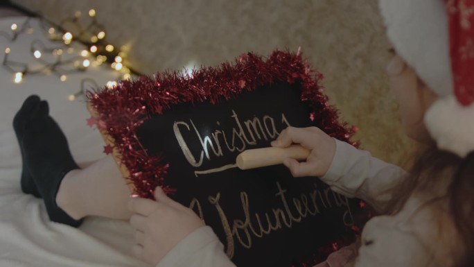 一个小女孩举着黑板，上面写着“圣诞节志愿服务”。圣诞志愿概念。