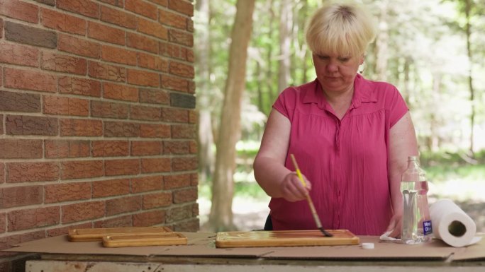 妇女用矿物油处理木质砧板。成熟的妇女在室外车间用矿物油制作菜板防水。