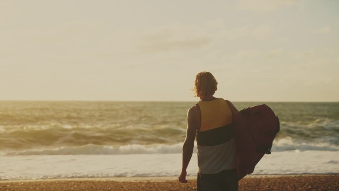 男冲浪者带着冲浪板在阳光明媚的海滩上观看海浪