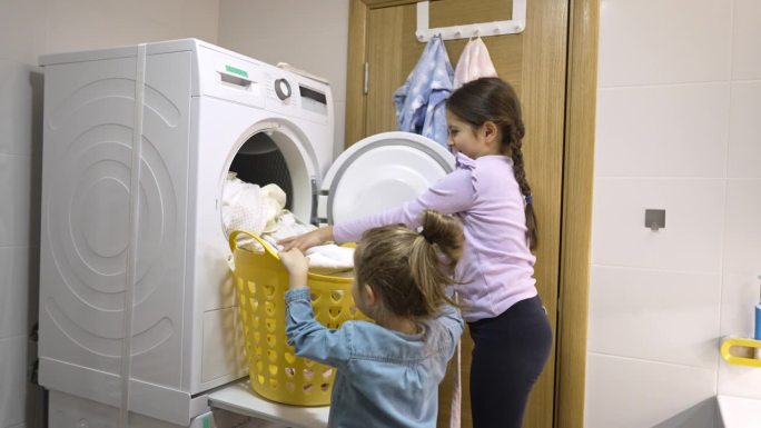 小女孩把衣服从烘干机里拿出来放进篮子里，她的妹妹帮着她