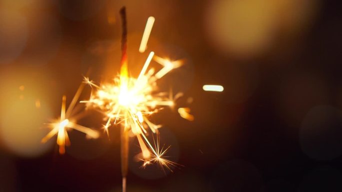 金色散景背景上的闪电火花特写，孟加拉灯正在燃烧，生日或新年夜的晚会。节日快乐。