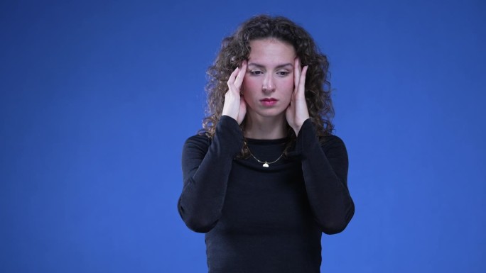 压力大的女人用手摸太阳穴平静自己，感到痛苦和头痛。与精神焦虑作斗争的人站在蓝色背景上