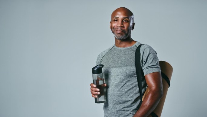 工作室肖像成熟的男人在健身房健身服装与运动垫和水瓶