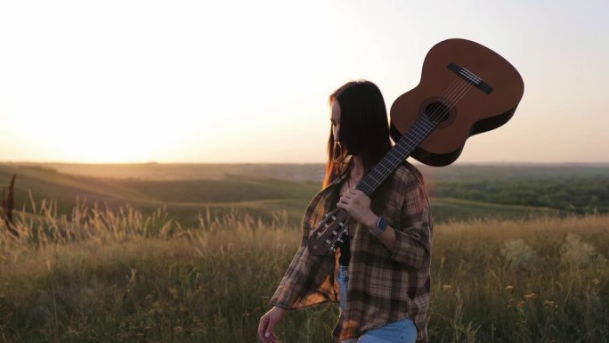 美丽的年轻女子在日落时分弹吉他。日落时分，女音乐家拿着吉他。