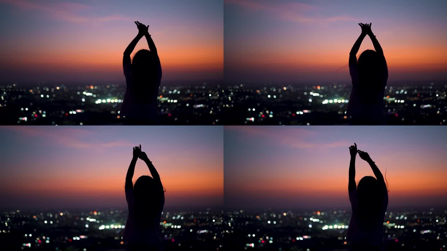 印度女孩在落日的余晖中举手，背景是这座城市的剪影。欣赏城市夜景的女游客。