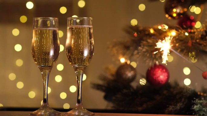 庆祝新年前夜的派对上有孟加拉灯和香槟，背景是圣诞树和闪烁的灯泡花环的散景。寒假，节日心情，祝酒