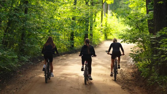 妇女骑自行车在地面道路上的森林，后景，慢镜头在大自然中，保持健康