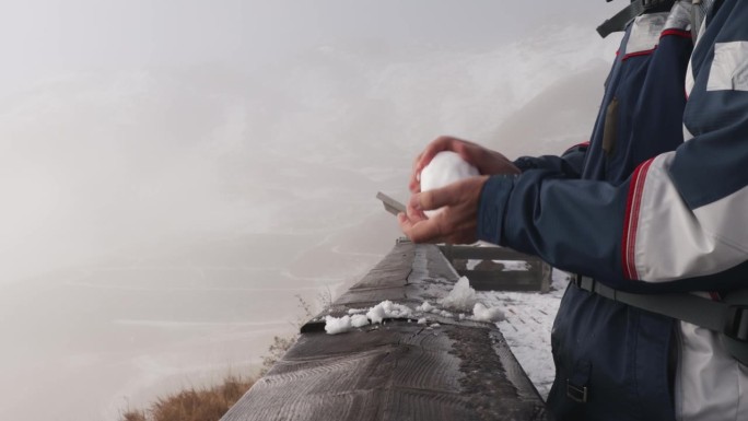 男人们的手在木栏杆上滚动着一个雪花玻璃球，背景是雾中的山脉
