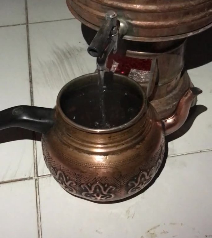 木头上的土耳其茶炊。一个男人用茶壶泡茶。热量是可见的。外面是晚上。垂直视频。