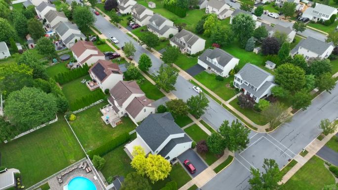 夏天的美国社区。空中旋转显示的广阔的住宅开发与绿树成荫的街道。住宅区的太阳能电池板和草坪。