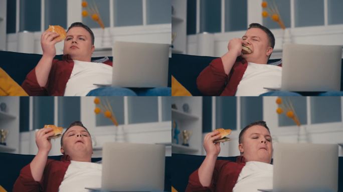 不整洁的超重男子吃着油腻的垃圾食品，坐在沙发上用笔记本电脑