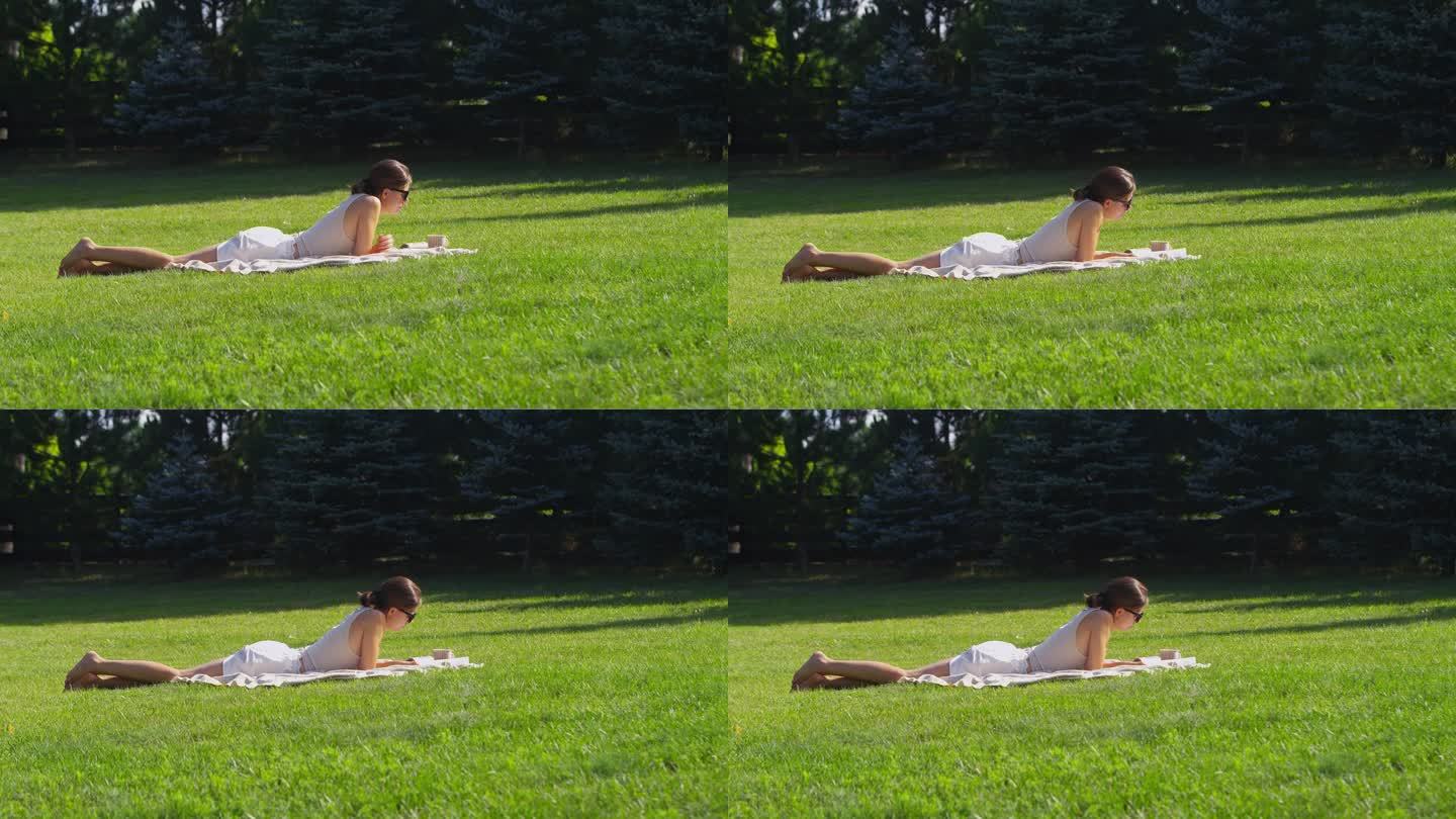在绿草地上休息的女人。在公园里读一本书，喝一杯热茶放松一下