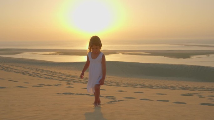 一个美丽的小女孩，穿着白色的裙子，赤脚走在沙滩上，夏日的黄昏，金色的夕阳映衬着大海，温暖的风吹皱了她