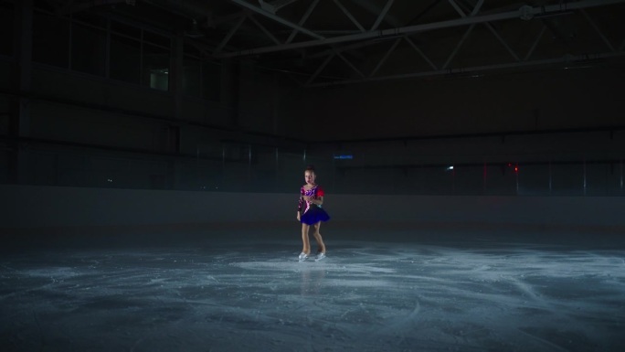 花样滑冰小女孩在运动场黑暗的溜冰场上训练表演花样