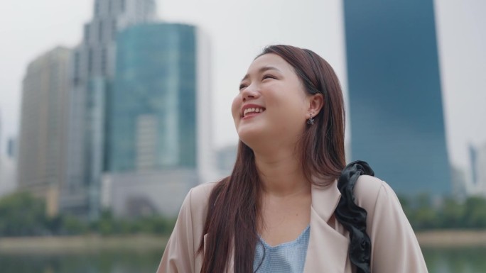 快乐的年轻亚洲女性站在户外看城市景观。自信快乐美丽的年轻女子仰望城市街道，梦想，思考或美好的未来。生