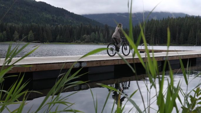 年轻女子沿着湖上的木码头骑自行车