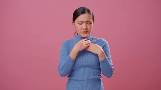 亚洲妇女发烧，流鼻涕，喉咙痛，孤立站在粉红色的背景上。