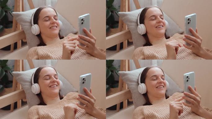 微笑的女人穿着针织毛衣，在家里的沙发上戴着耳机听音乐，浏览网页，在社交网络上交流。
