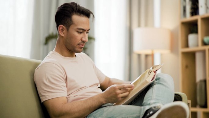 书，放松和亚洲男人阅读在沙发上与和平，轻松或在他的家寒心。有知识、有文学和日本男性的人在客厅里用小说