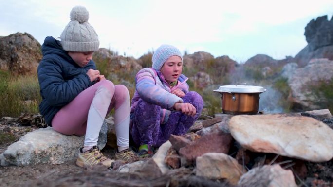 两个女孩在营火上烧着热水