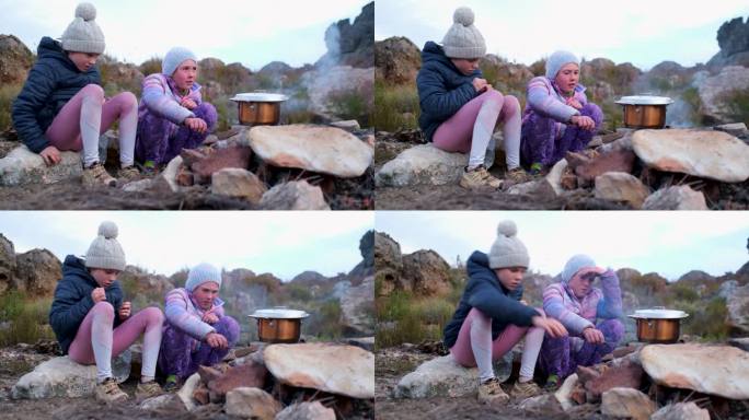 两个女孩在营火上烧着热水