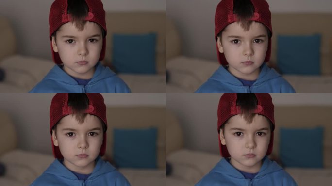 戴着红色棒球帽的严肃男孩看着室内的照相机。肖像可爱学龄前严重儿童严重沉思担心高加索少年。悲伤自信的小