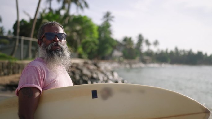 带着冲浪板走在沙滩上的老年男性旅行者，拥有积极健康的黄金生活方式，放眼四周，乘着小船欣赏海湾美景，异