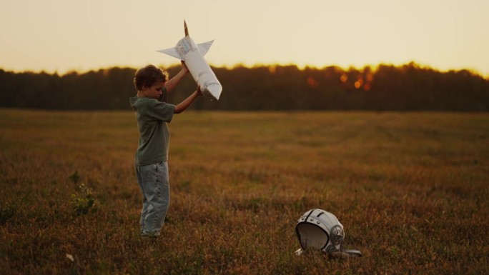 大自然中的小男孩，夏天在田野里玩玩具火箭和太空头盔的孩子，慢镜头