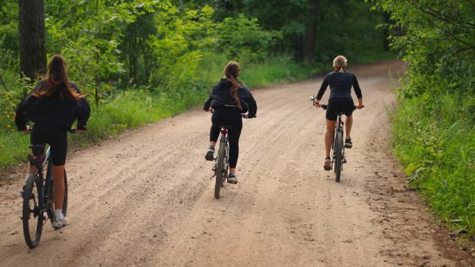 十几岁的女孩骑自行车在森林，后视图，以下镜头，慢动作，运动和积极的生活方式