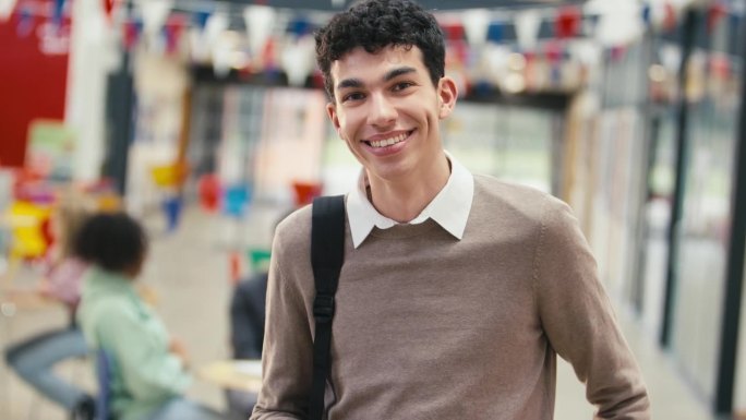 微笑的男大学生站在大学大楼里用手机的肖像