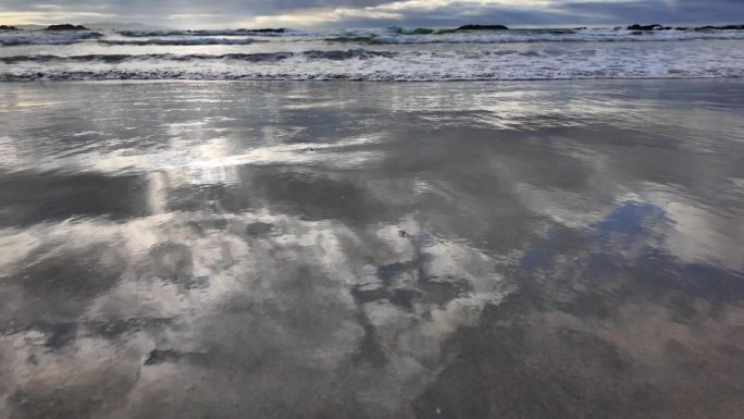 海浪翻滚到沙滩上，背景是蓝色的天空，有戏剧性的雷云，日落，美丽的风景，慢动作