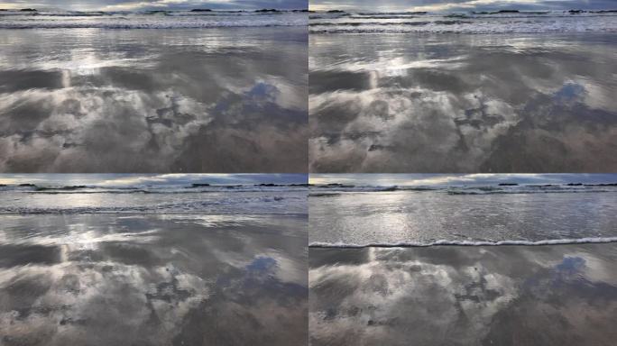 海浪翻滚到沙滩上，背景是蓝色的天空，有戏剧性的雷云，日落，美丽的风景，慢动作