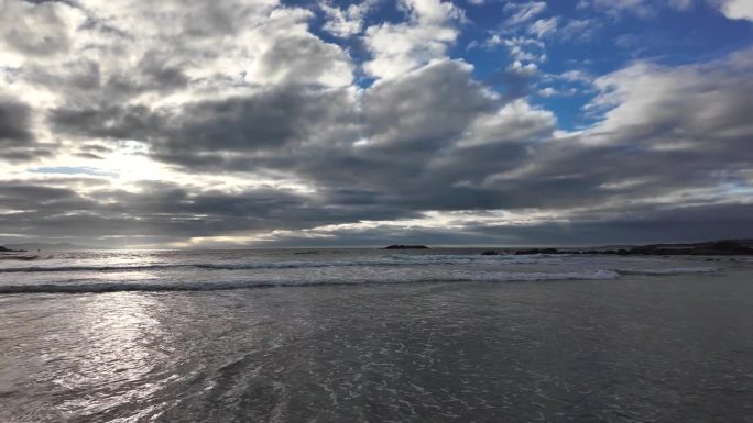 海浪翻滚到沙滩上，背景是蓝色的天空，有戏剧性的雷云，日落，美丽的风景，慢动作