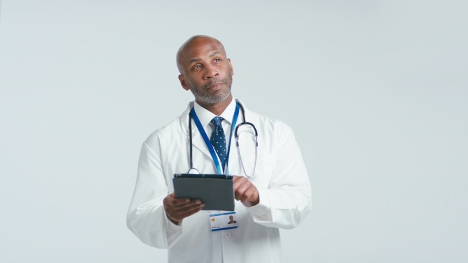 成年医生穿着白大褂，在白色背景下用数码平板电脑拍摄