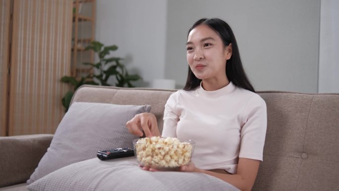 亚洲年轻漂亮的女人在家里看有趣的电视电影。有吸引力的休闲女孩感到快乐和放松。