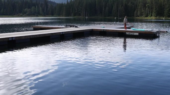 女子在宁静的湖码头吹桨板(SUP)