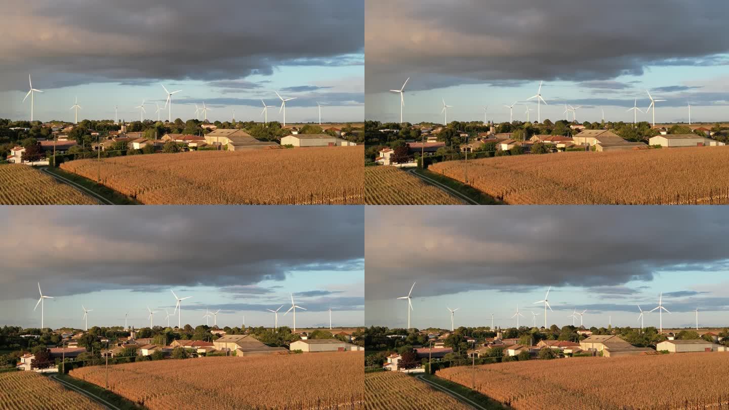 风力涡轮机在蓝天的映衬下转动，天空上是深灰色的风暴云，雨在法国村庄的视线之下。