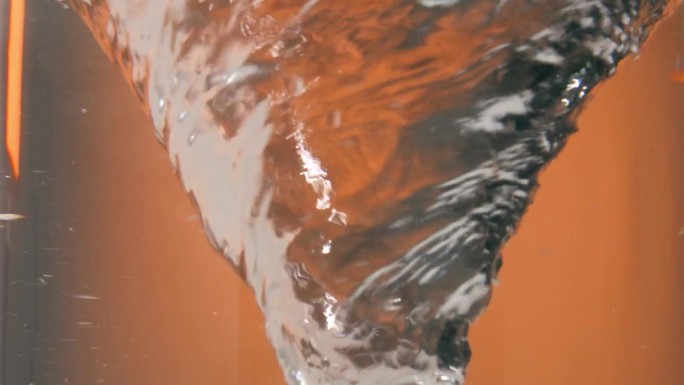 一个旋转或盘旋的水漩涡或水龙卷风在橙色背景前的静态慢动作镜头