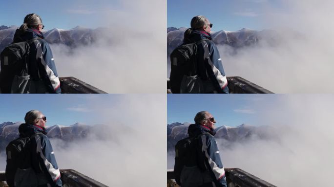 一个头发花白、戴着墨镜的男人站在群山的高处，看着移动的云