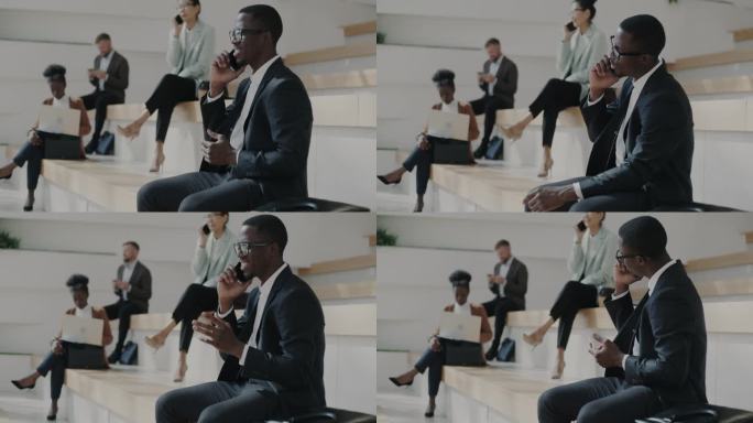 快乐的非裔美国商人坐在办公大楼附近的楼梯上，用手机交谈，竖起大拇指