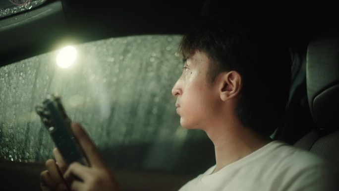 男子下雨天在车里玩智能手机。