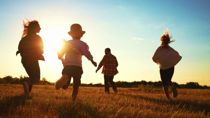回头看幸福的一家人一起欢欢喜喜地奔跑在夏日的田野草地上。休闲活动，漫步大自然。孩子和父母。运动的运动