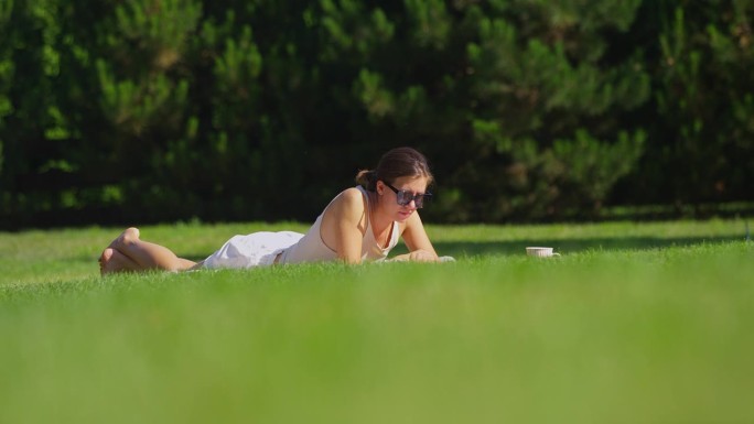 在草地上休息的女人。在公园里读一本书，喝一杯热茶放松一下