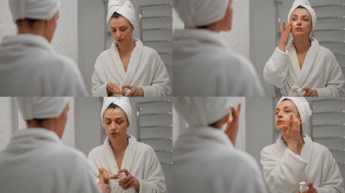 女士使用保湿泡沫洗脸和微笑，早上的护肤程序。年轻的女学生头上缠着毛巾，在水疗沙龙照镜子。准备化妆。