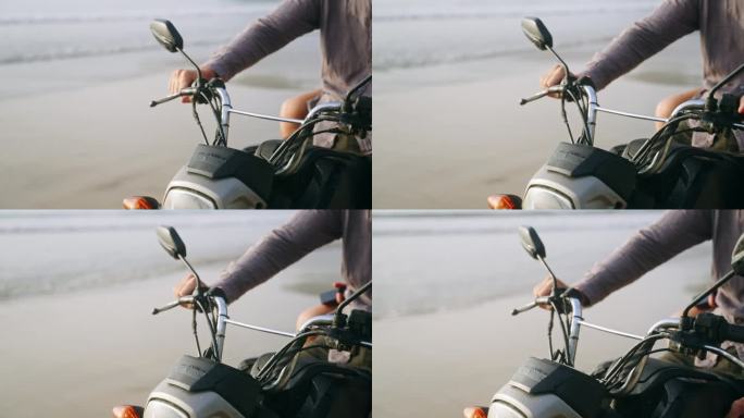 海边骑摩托车的人把手放在摩托车车把上。一个人在海边拿着摩托车把手。摩托车仪表盘，后视镜。一个人坐在海