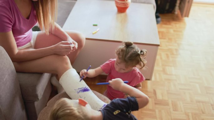 母亲和她的两个孩子在腿上的石膏上写字